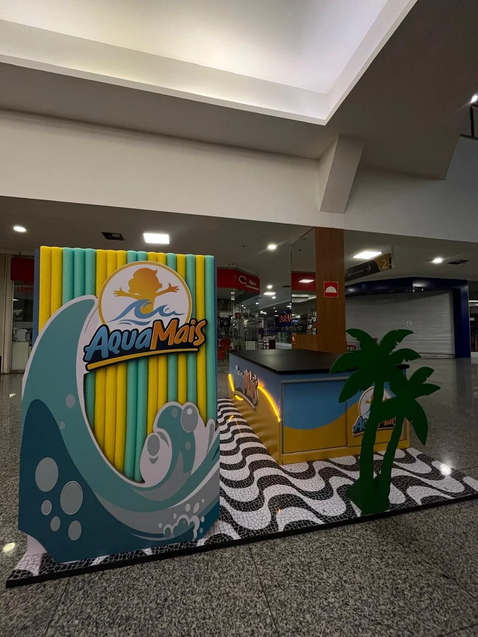 Cenografia com painel em forma de onda, piso de pedras portuguesas e coqueiros cenográficos, em shopping