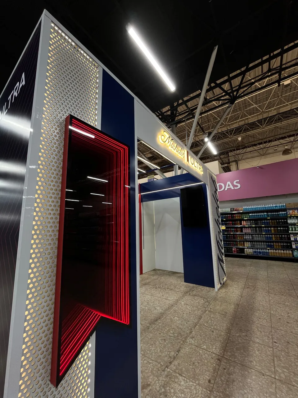 Portal de marca em supermercado, com painel perfurado iluminado e espelho com contorno vermelho em LED