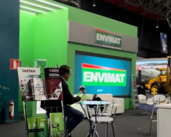 Estande com estrutura verde, letreiro iluminado e telão, em pavilhão de feira